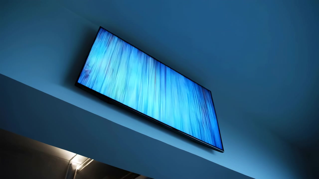 High angle interior view of wall mounted television beneath broad ceiling ledge, screen glowing with abstract blue texture and fine noise pattern, set within modern minimal room with cool ambient