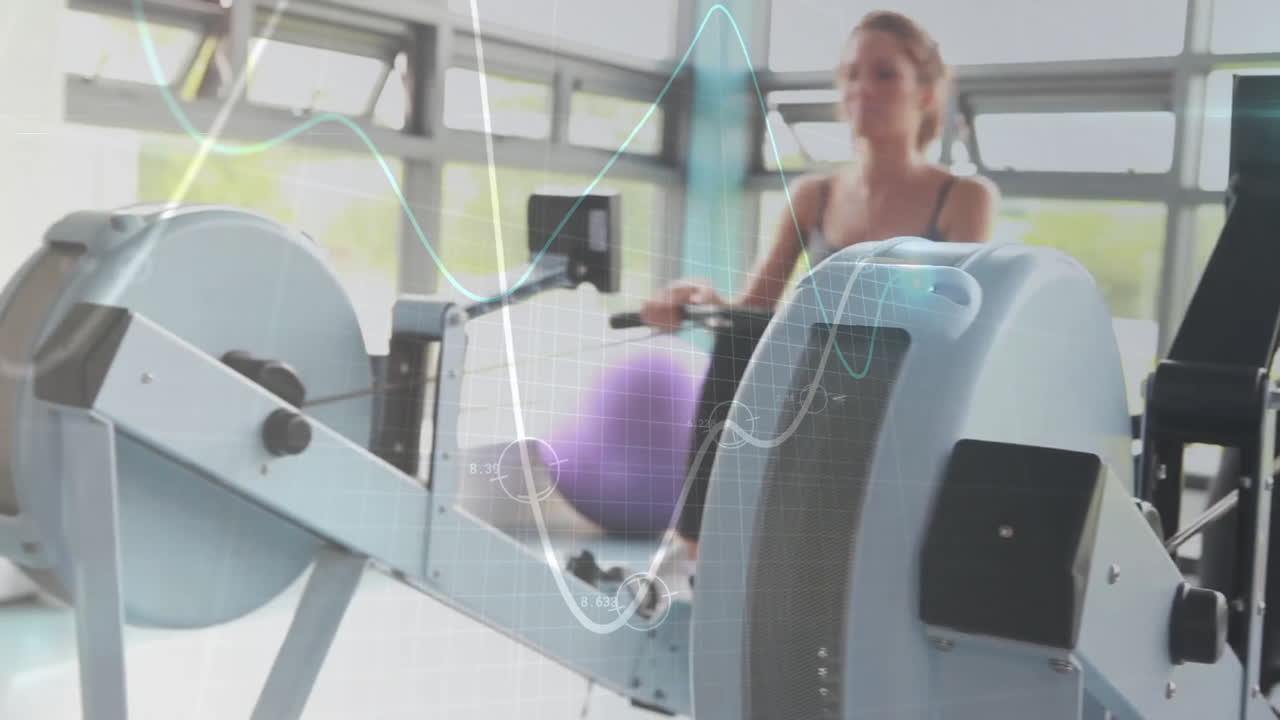 Two women pulling rowing machine handles in fitness studio, displaying floating exercise ball icon