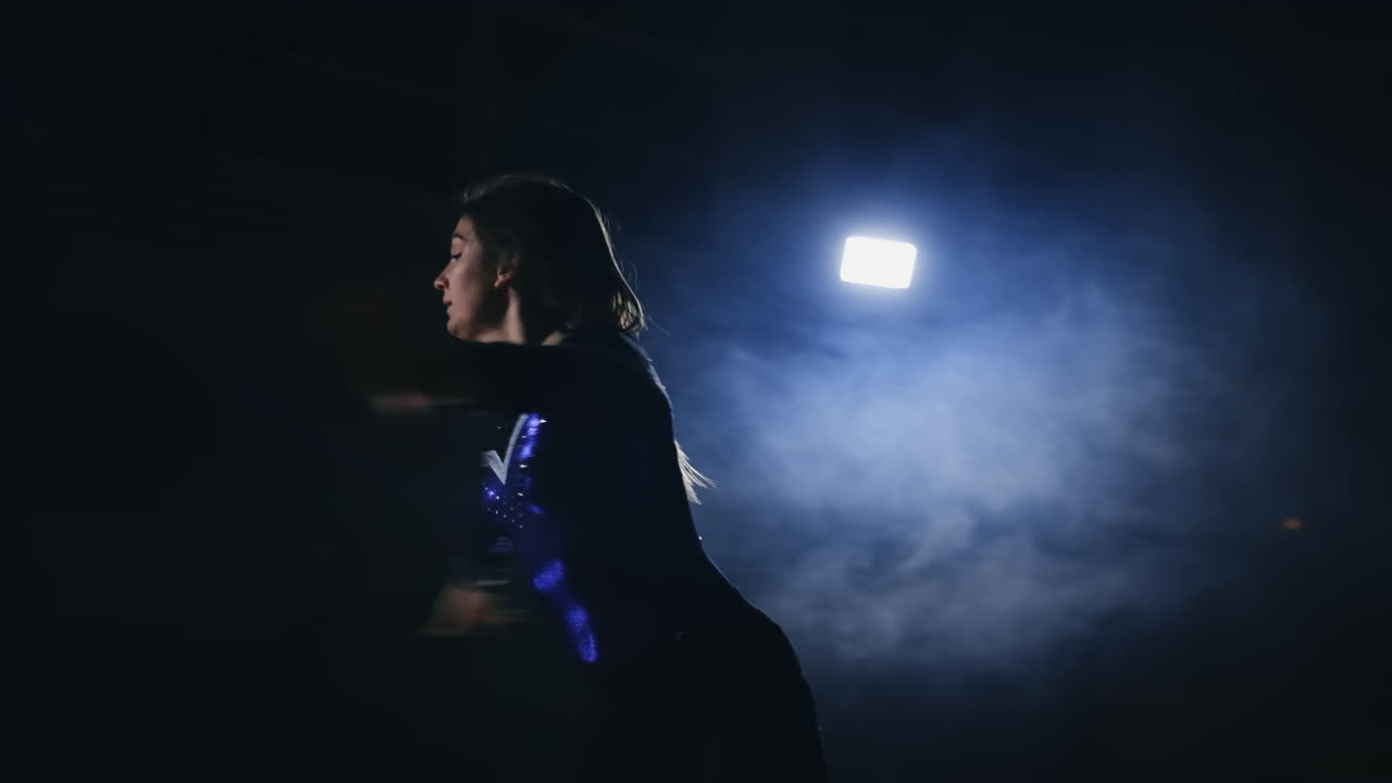 la niña realiza una rotación en la gimnasia artística en un fondo oscuro en el humo en cámara lenta