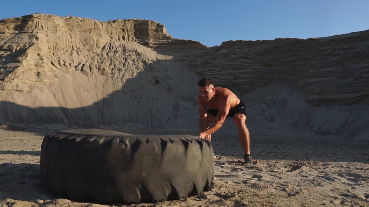 atleta muscular hombre fuerte golpea un martillo en una rueda enorme en las montañas arenosas en cámara lenta. entrenamiento de fuerza y resistencia para luchadores