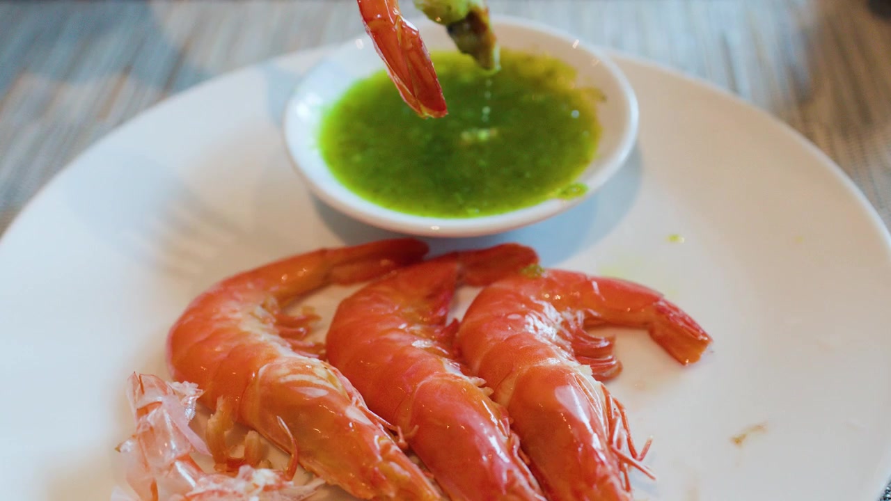 Una forchetta raccoglie un gambero bollito e lo intinge in una salsa di frutti di mare verde piccante