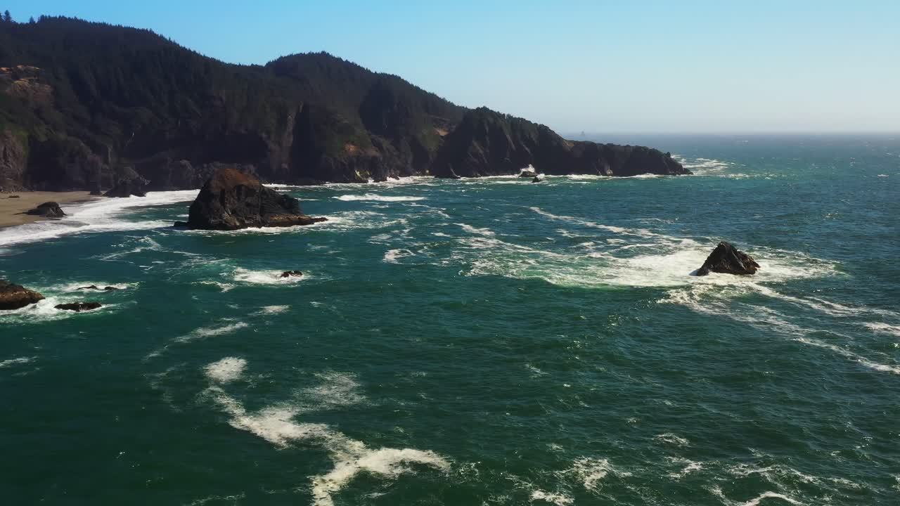 Scenic aerial shot over an ocean waves and sea stacks in the water on the rocky coast of Oregon, Pacific Northwest.