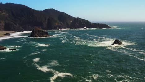 scenic aerial shot over an ocean waves and sea stacks in the water on the rocky coast of oregon, pacific northwest.