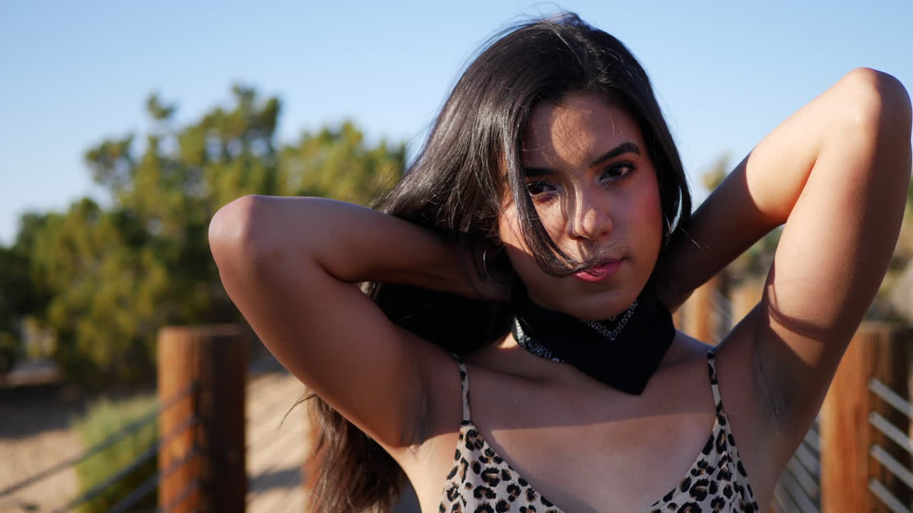 una hermosa joven modelo hispana atando un pañuelo y mirando en un paisaje desértico al aire libre a cámara lenta