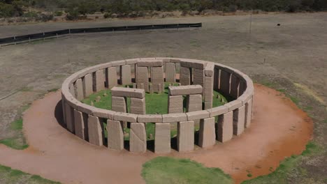 Excelente-Toma-Aérea-De-Un-Hombre-Sentado-En-La-Réplica-De-Stonehenge-En-Esperance,-Australia