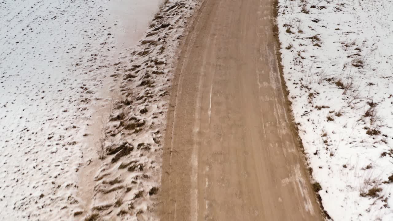 Flying low over a gravel road in winter and tilting upwards to revel the scenery. Aerial overhead view of a winding road through the countryside.