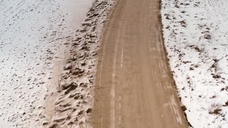 flying low over a gravel road in winter and tilting upwards to revel the scenery. aerial overhead view of a winding road through the countryside.