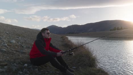 joven con chaqueta roja pescando sentado en un río tranquilo durante el atardecer