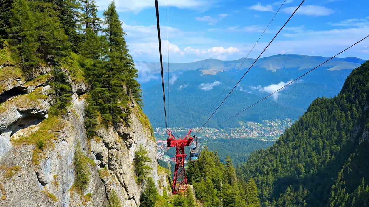 Cable car view over a mountain valley town. The red gondola structure frames a scenic look down at the forest and city below