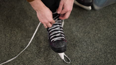 close-up of hands loosening the lace of a black ice skate with red accents on a gray carpeted floor