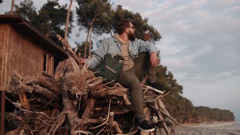 man sitting on a pile of driftwood by the beach