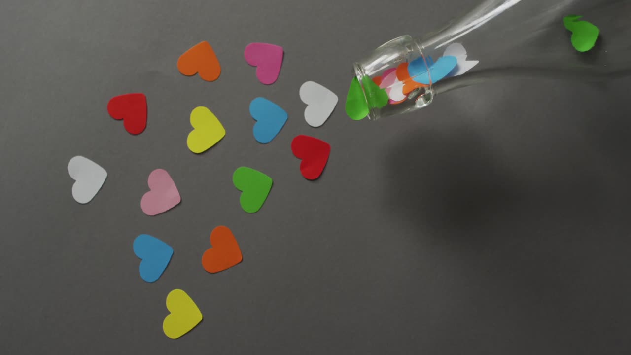 Colourful paper hearts and bottle on gray background at valentine's day