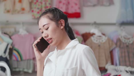close up of asian mother talking on smartphone while choosing kids clothing items on hangers at the boutique