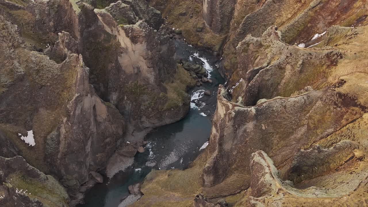 Top-down drone view of Fjaðrárgljúfur Canyon in Iceland, highlighting the deep river gorge cutting through dramatic rocky cliffs in a rugged landscape.