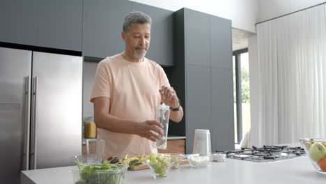 Feliz-Hombre-Birracial-Mayor-Preparando-Batidos-Saludables-En-La-Cocina-De-Casa,-Espacio-Para-Copiar,-Cámara-Lenta