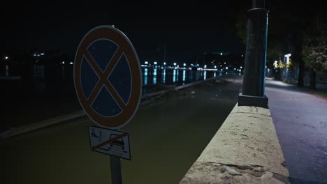 sign prohibiting stopping near a flooded riverside walkway in Budapest at night