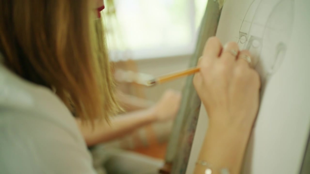 Giovane studente d'arte che disegna uno schizzo di ritratto su carta montata su un cavalletto durante un laboratorio in classe.