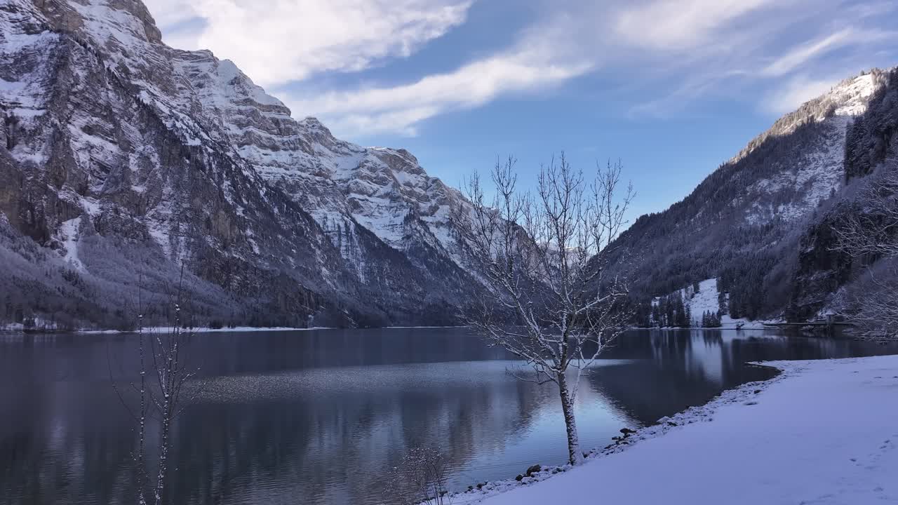 A calm snowy lake surrounded by tall mountains and a clear blue winter sky