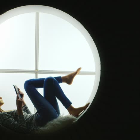 woman sitting in a round window uses tablet