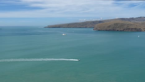 Eastern-part-of-extinct-volcano-slopes-into-ocean-as-boats-head-towards-harbor---Adderly-Head,-Banks-Peninsula