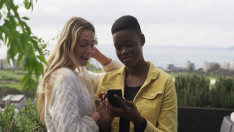 mujeres jóvenes usando un teléfono inteligente en un techo