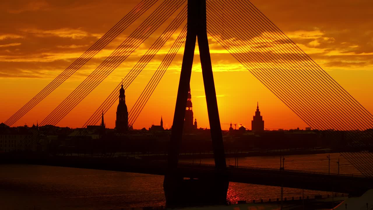 Cinematic drone view shows glowing sun behind Old Riga and Vanšu Bridge cables