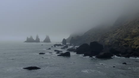 aerial cinematic slow path backward waves crashing haystacks at vik iceland early winter fog at black sand beach