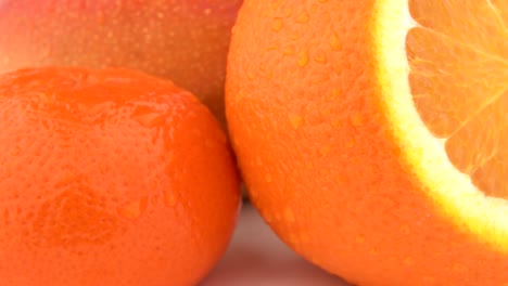 macro de mango, frutas de naranja y frutas de mandarina con gotas en la piel. girando sobre fondo blanco. aislado.