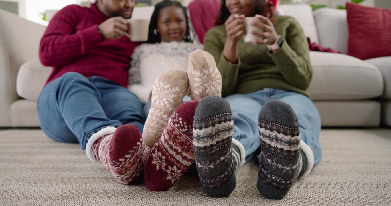 Afroamerikanische Familie auf dem Teppich, Kind wackelt mit gemusterten Socken, Eltern lächeln und trinken aus Tassen