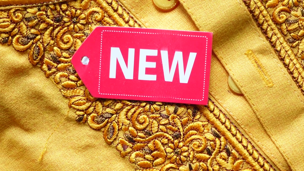 Close-up of a Red 'NEW' Tag on Golden Embroidered Yellow Fabric