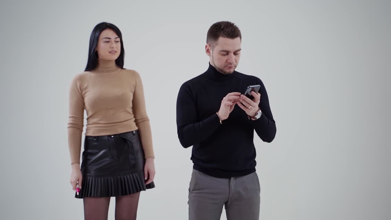 Portrait of a couple in the light studio. Handsome man looking into his cell phone. Beautiful woman coming to a man. Slow motion.