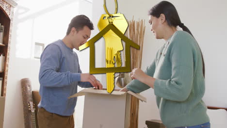 animación de la llave de la casa de oro y el llavero sobre una pareja biracial desempaquetando cajas moviéndose a una nueva casa