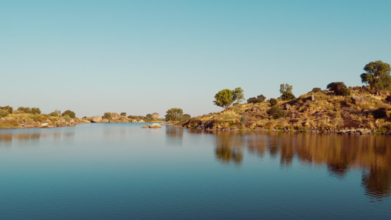 Água tranquila refletindo uma encosta ensolarada com árvores