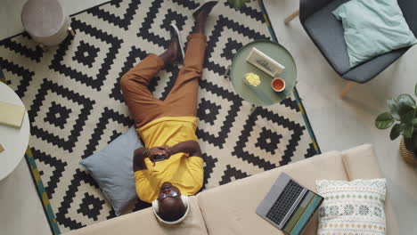 black man in headphones sitting on floor and using smartphone