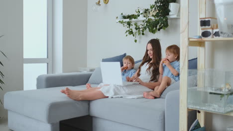 beautiful young mom and two little kids boys are looking at the laptop screen family photos. and they do online shopping. call grandma via video chat