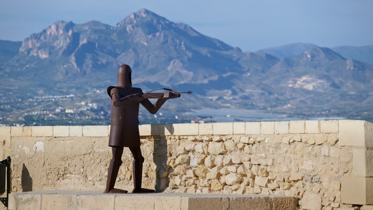 Steel sculpture of a medieval crossbowman on the Santa Barbara Castle parapet, city and mountains on the background