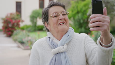 Retrato-De-Una-Anciana-Feliz-Tomando-Fotos-Usando-La-Cámara-Del-Teléfono-Inteligente-Disfrutando-De-Un-Día-Soleado-Al-Aire-Libre-En-El-Fondo-Del-Jardín-Usando-Bufanda