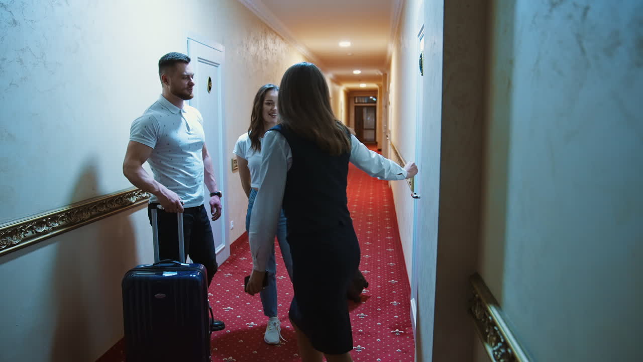 Ungt par går på hotelgang. Par med rejsetasker går langs hotelkorridor