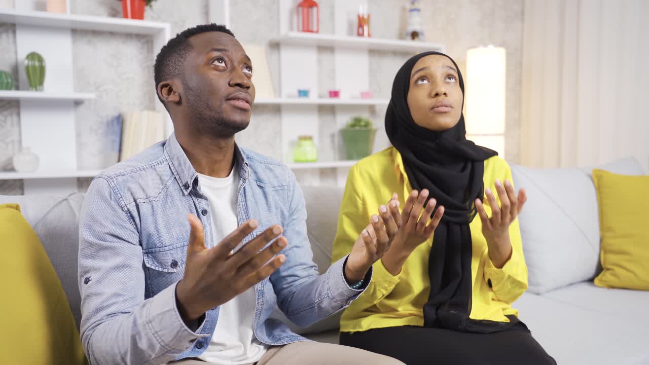 Pasangan suami istri Muslim Afrika sedang berdoa di rumah, menengadahkan tangan mereka kepada Allah.