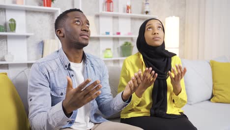 muslim african married couple praying at home, opening their hands to allah.