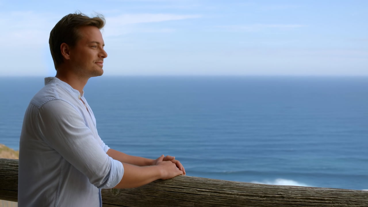 Caucasian Man Gazing At Ocean Hands Resting On Wooden Railing Overlooking Coastal Bluff Casual White Shirt