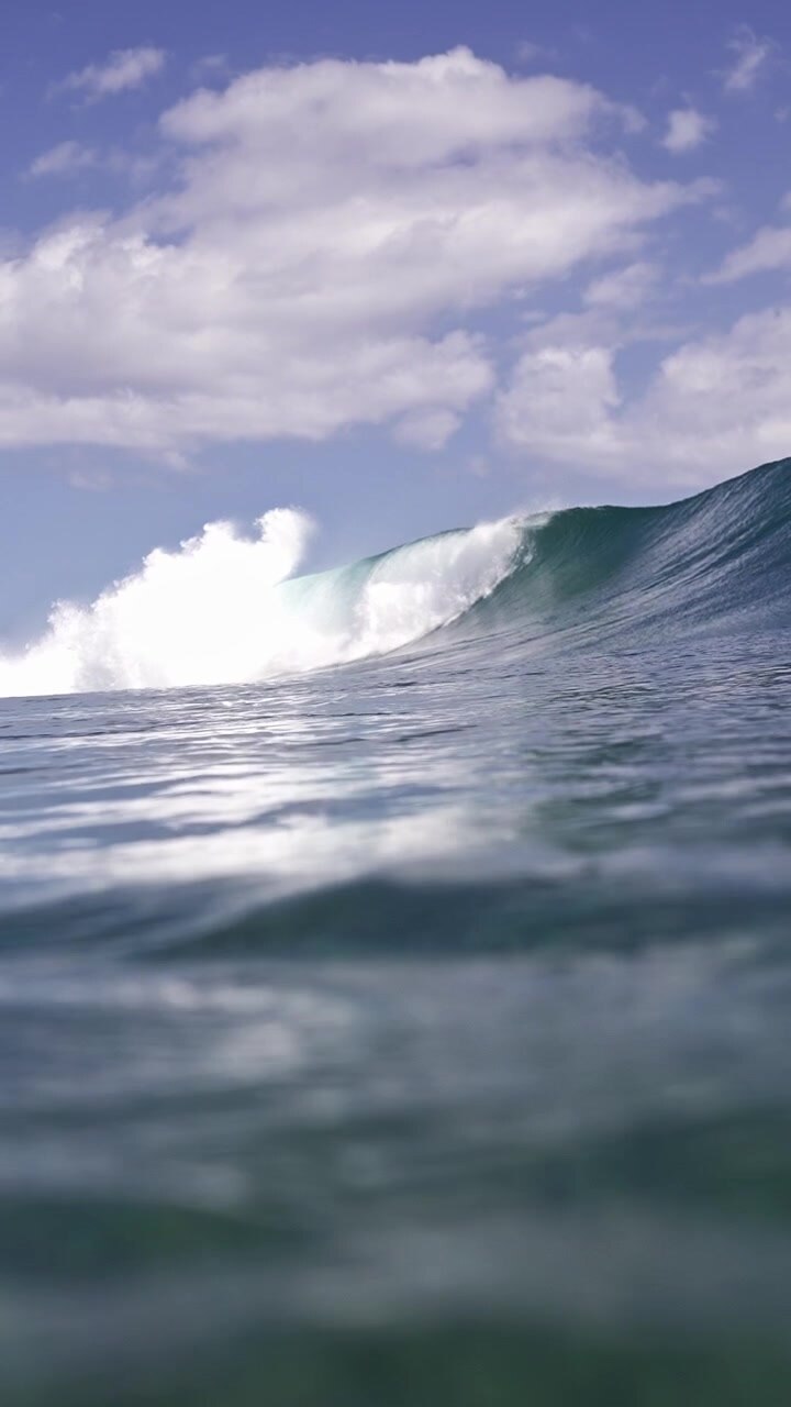 Large ocean waves rise and fall beneath a sky dotted with clouds, creating a dramatic seascape. Suitable for use in marine documentaries or surf-related projects.