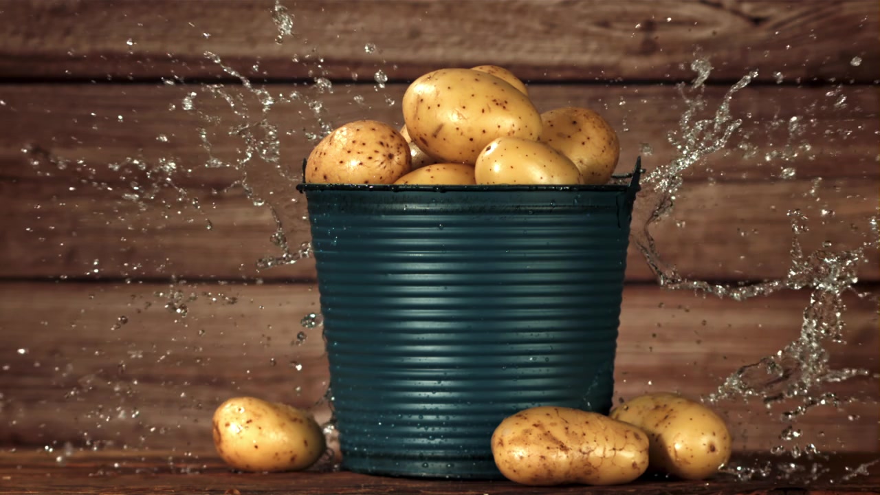 Patate fresche crude in un secchio con acqua che schizza