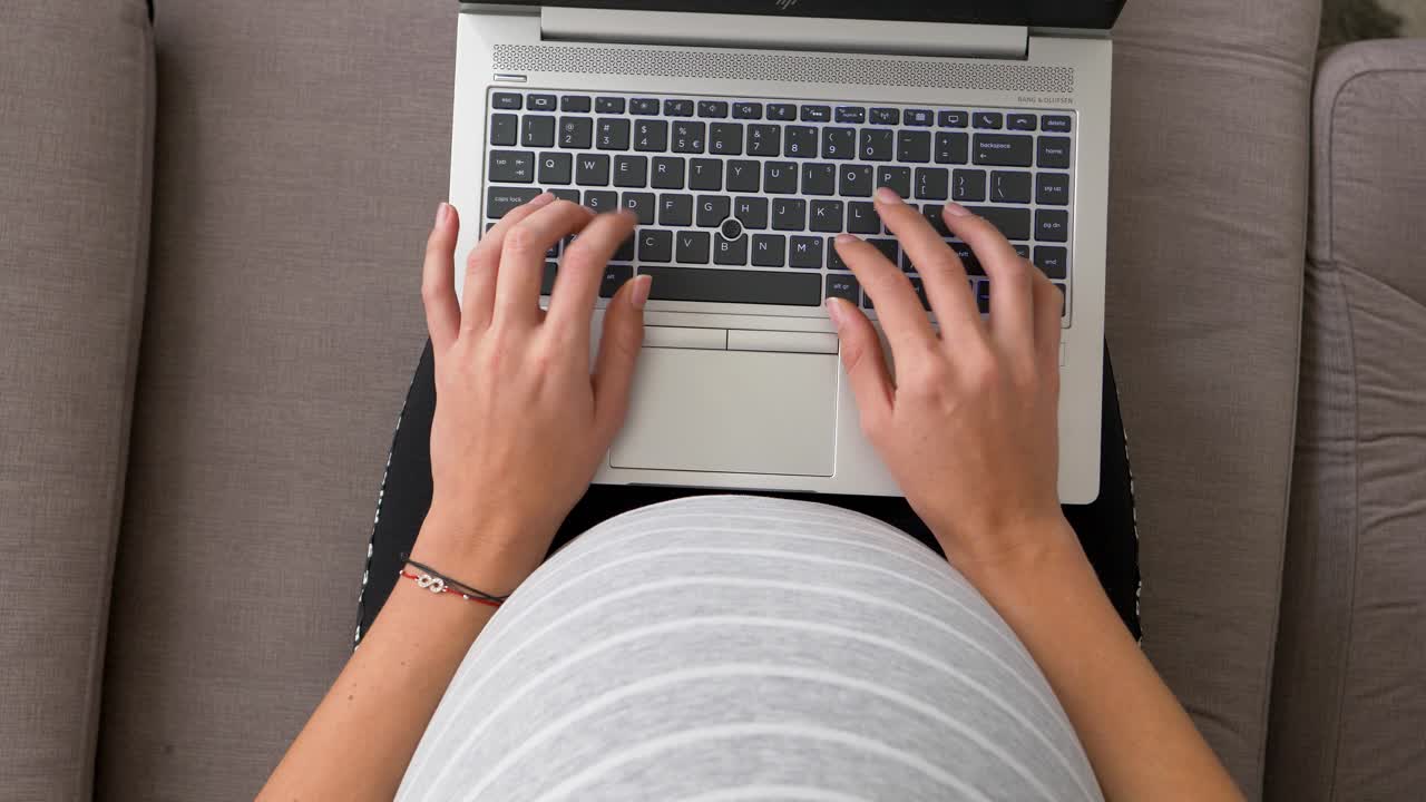 woman works on laptop sitting on couch during last trimester pregnancy