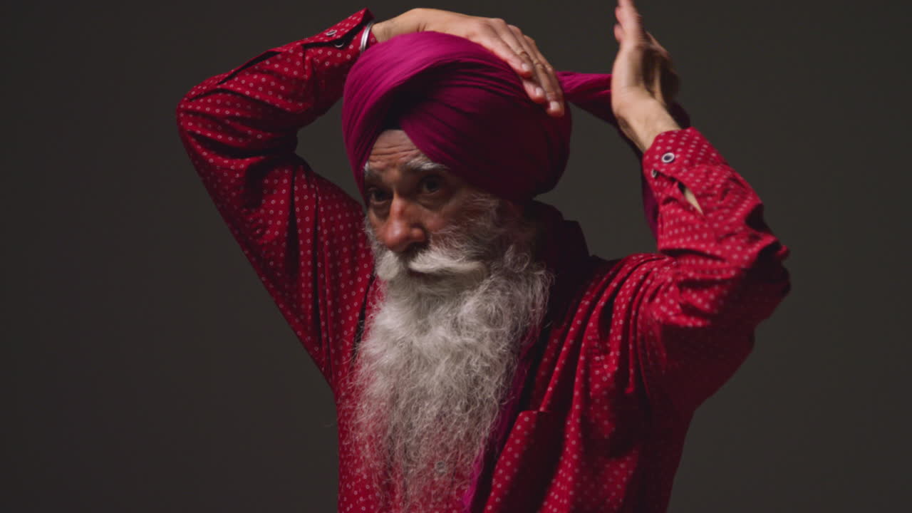fotografía de iluminación de estudio de baja clave de un hombre sikh anciano con barba atando tela para turbante contra un fondo oscuro 14
