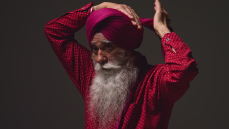 low key studio illuminazione scatto di anziano sikh uomo con la barba legando tessuto per turban contro lo sfondo scuro 14