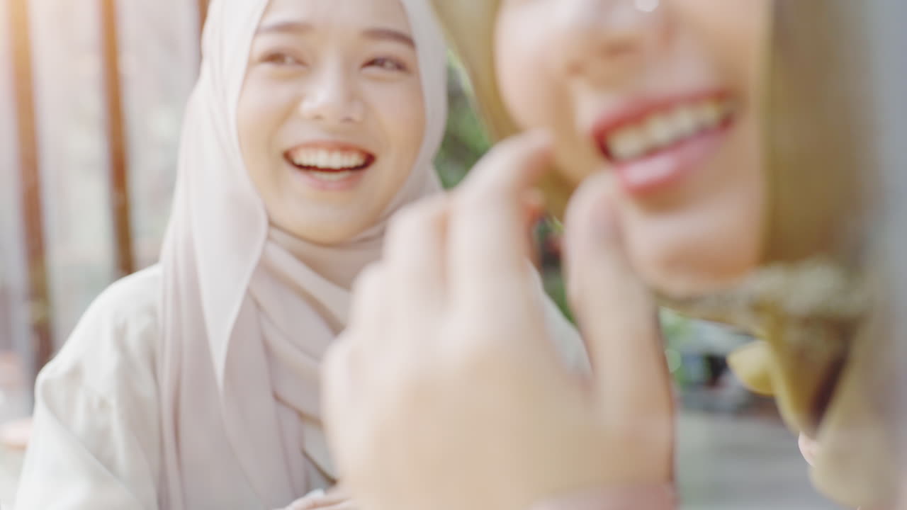 아름다운 젊은 아시아 무슬림 여성들이 고 은 날에 커피에서 휴대전화로 일하고 놀고 휴식을 즐기고 있습니다.