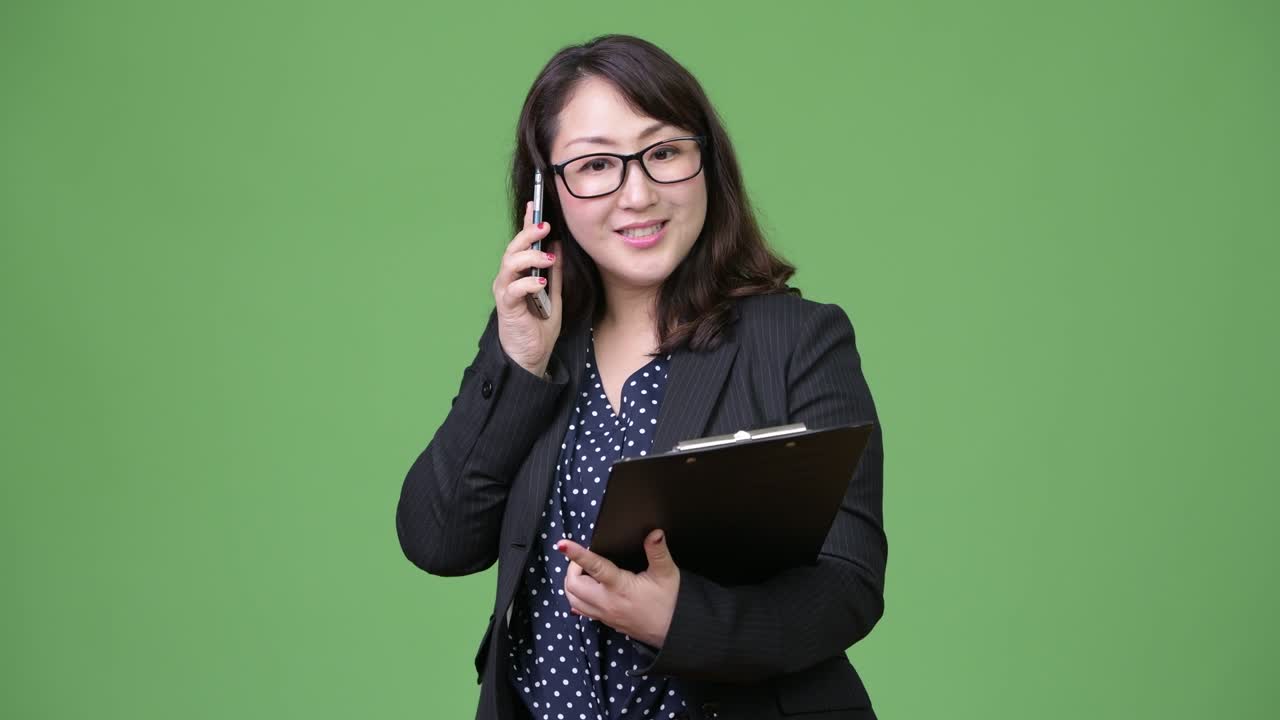 una hermosa mujer de negocios asiática madura usando el teléfono mientras sostiene el portapapeles