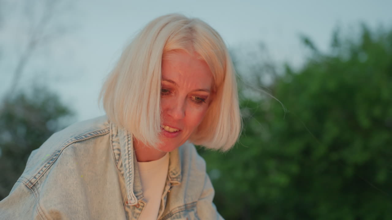 close up female artist painting lifts head to admire vibrant brush strokes on paper under warm sunset light capturing moment of pride and inspiration during outdoor creative with serene backdrop