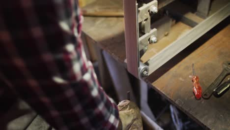 close up of hands of caucasian male knife maker in workshop using sander